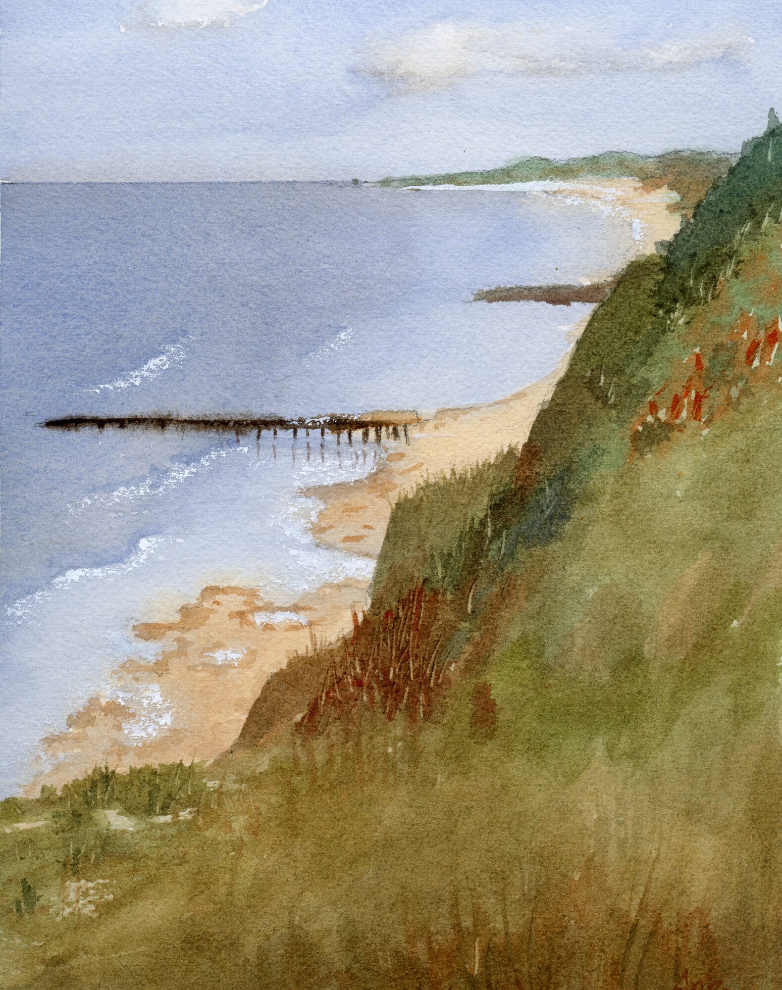 a sandy beach and coastline seen from a grassy hilltop, with a low stone breakwater reaching into a calm sea